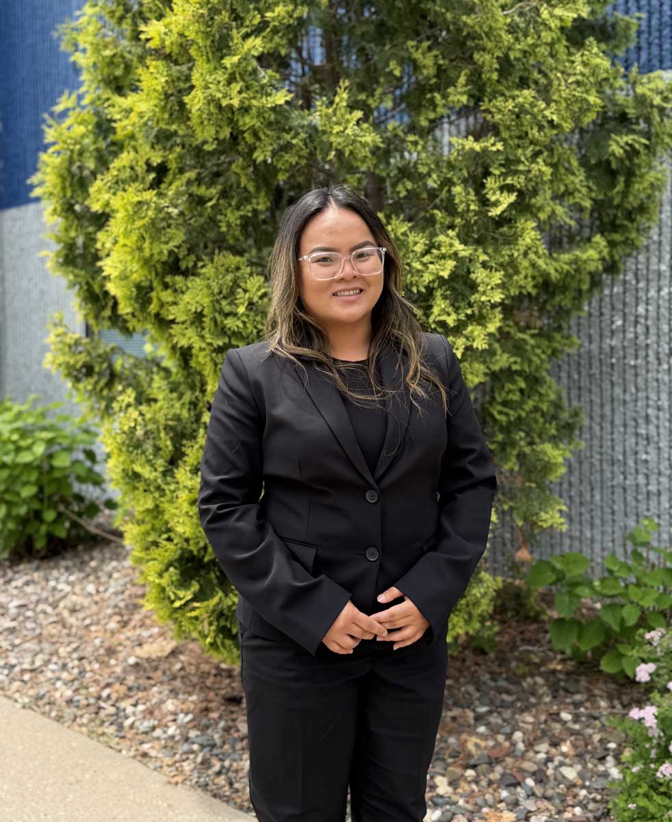 Woman in black suit standing outdoors by greenery