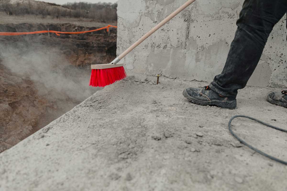 Worker Sweeping Concrete On Construction Site